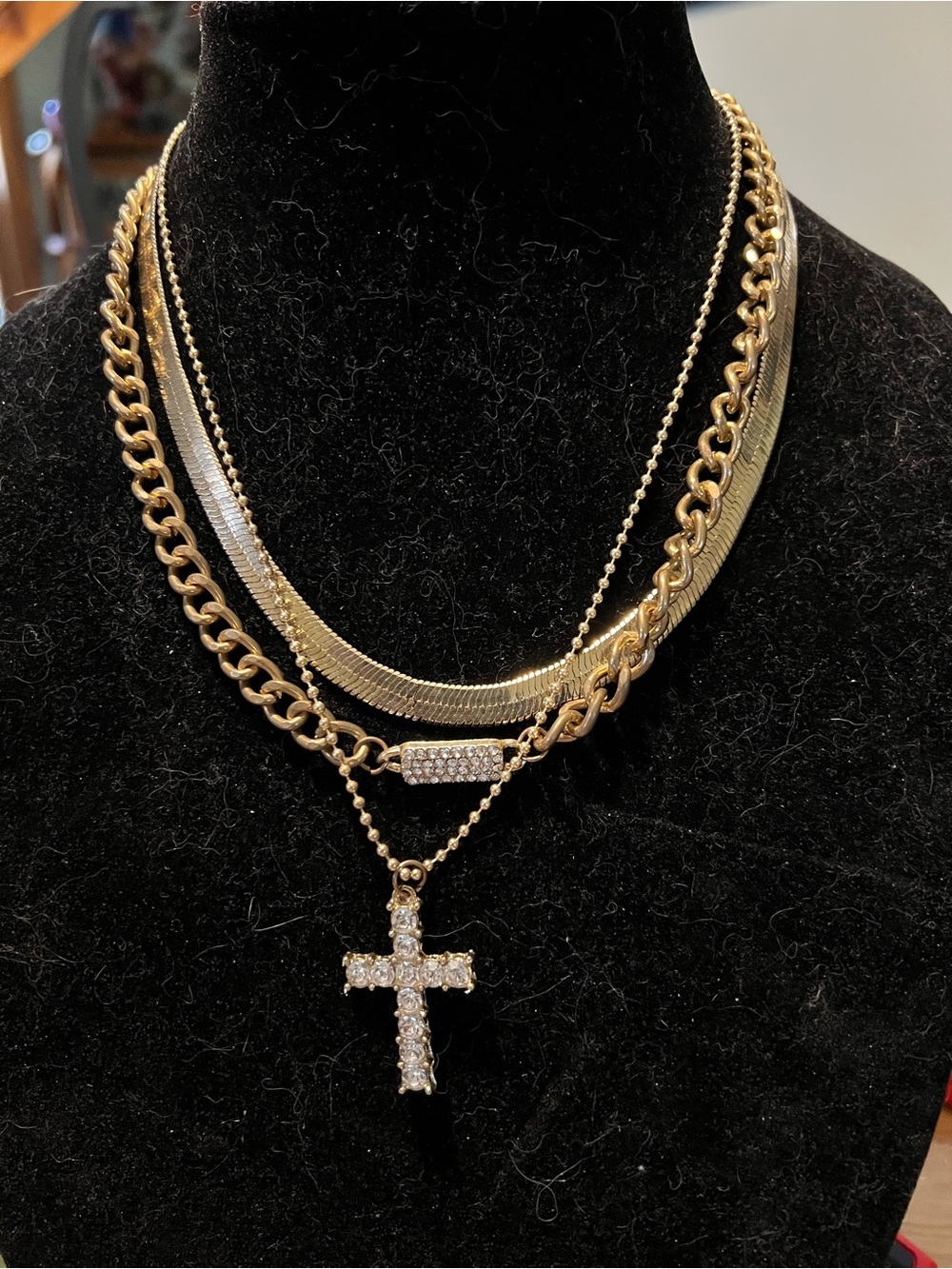 Multi-layered gold tone chain necklace with herringbone, curb link, and cross.